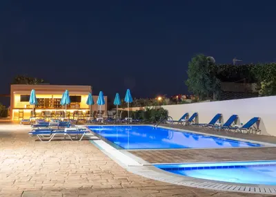 a swimming pool at night with chairs and umbrellas at Amaryllis Beach House in Lardos