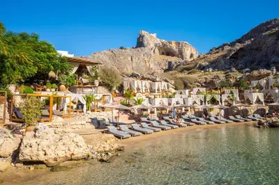 a beach with chaise lounges and chairs and a mountain at Villa Livis 1 in Kiotari