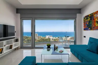 a living room with a blue couch and a large window at Rhodes Skyline Suite with out Door Jacuzzi Sea View in Ixia