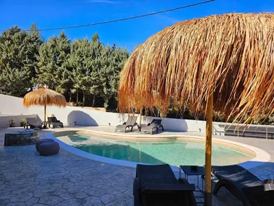 a swimming pool with a straw umbrella and chairs at Dream Luxury Apartment Suites in Pastida