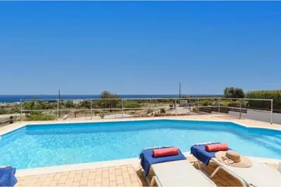 a large swimming pool with lounge chairs and the ocean at Villa Nicole Gennadi in Gennadi
