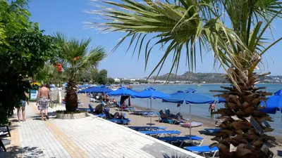 a beach with blue umbrellas and people on the beach at Avi Suites Faliraki in Faliraki
