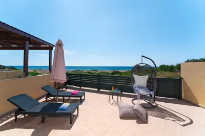 a patio with chairs and an umbrella and the ocean at Mare Blu 1 on the beach in Gennadi