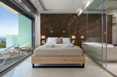 a bedroom with a large bed and a tub and a glass wall at Rhodes SkyLine Suites in Ixia
