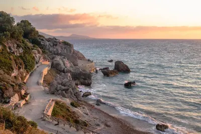 a beach with rocks and the ocean at sunset at Rodos Beach Apartment 33 in Rhodes Town