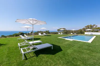 a lawn with chairs and an umbrella and a swimming pool at Aquarama Pool Apartments in Ixia